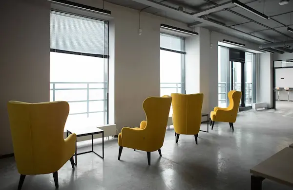 линейные офисные светильники на потолке и желтые кресла на фоне окон