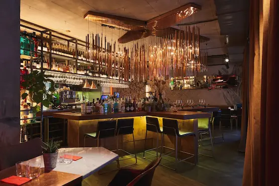 большая медная люстра авторского изготовления из множества подвесных трубочек в центре зала вечернего ресторана