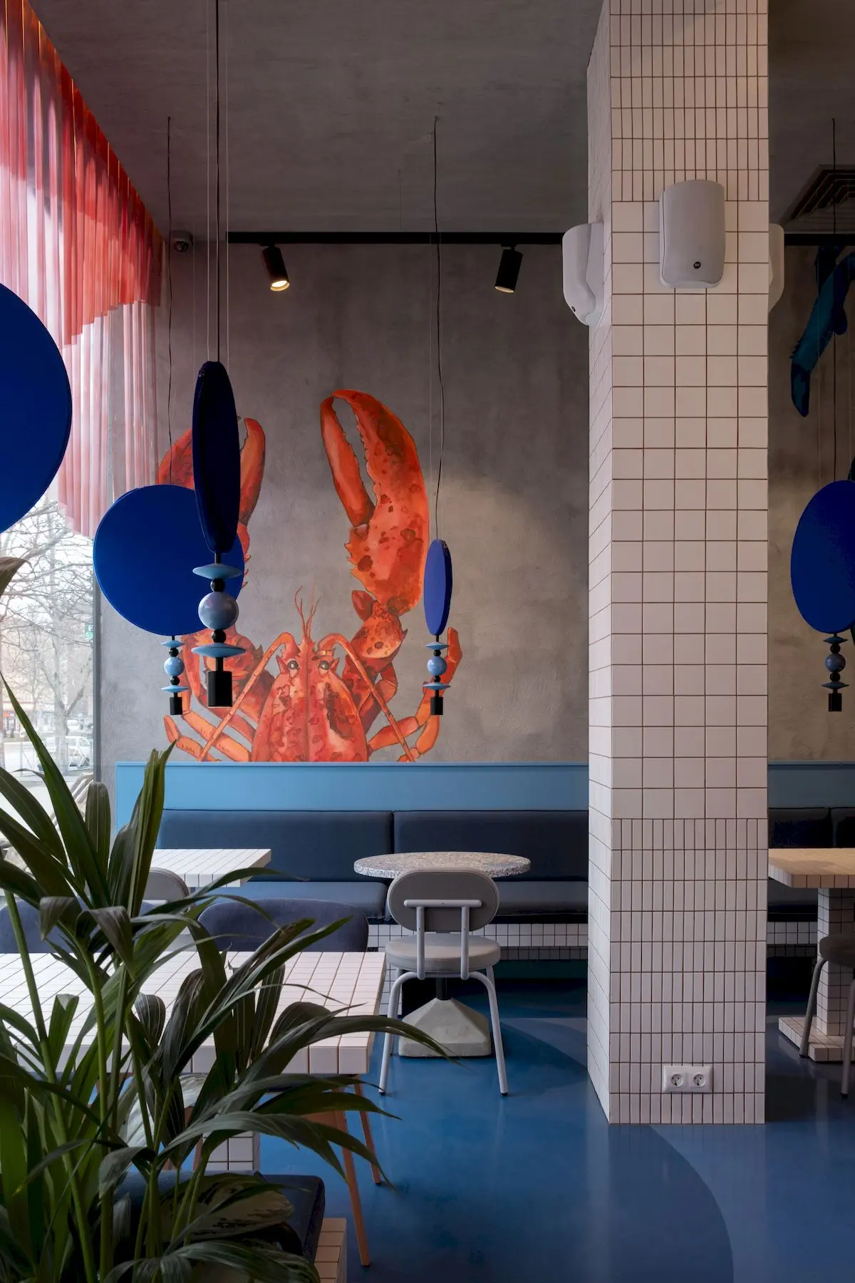 дизайнерские светильники голубого и синего цвета на фоне зеленых растений в ресторане с морской тематикой