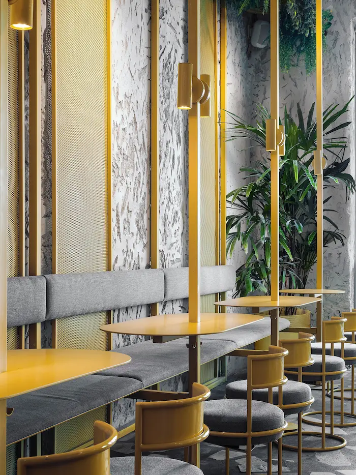 необычные дизайнерские светильники из металла светят над столиками в желтом интерьере ресторана на фоне зелени в Pobo